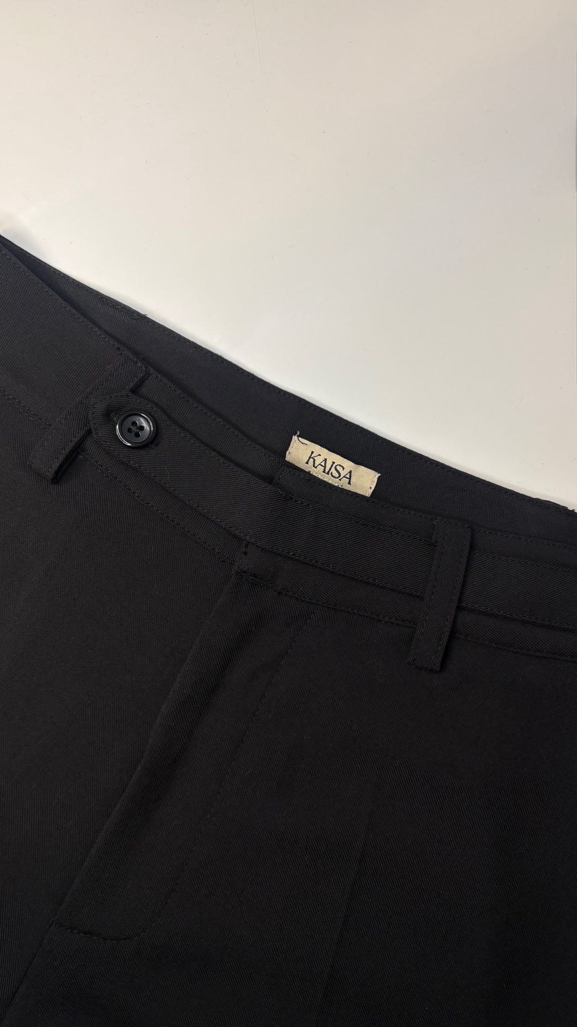 Close-up of Muse straight leg trousers in noir black showing waistband, button fastening and KAISA inside logo label