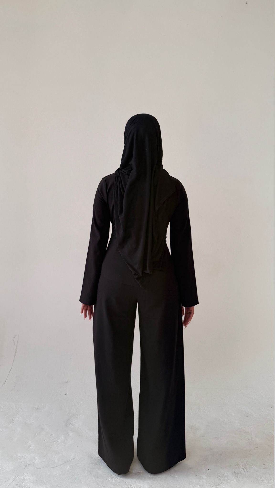 Model facing away showing back view of Muse tailored top in noir black, designed for petite frames with structured fit